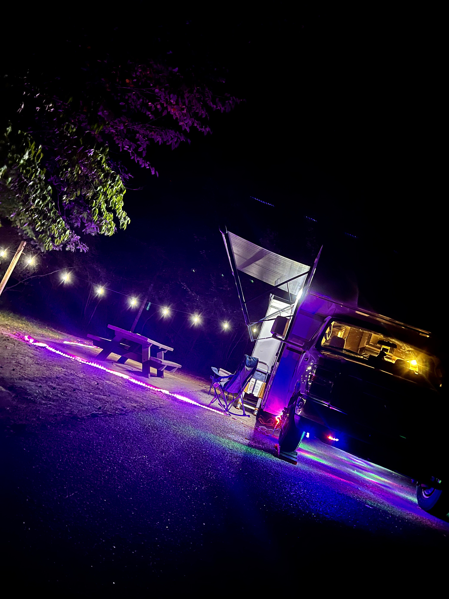 Nite photo of Lyric and David’s RV with purple LED lights and festoon lighting making it look like a festive night party scene. 