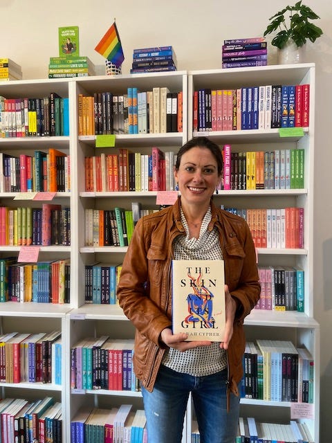 I'm cheesing with THE SKIN AND ITS GIRL in front of this beautiful rainbow of books at Little District Bookshop in Washington, DC!