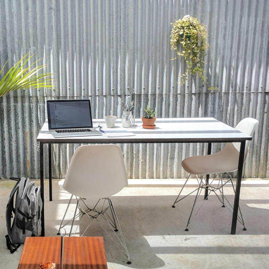 outdoor table and chairs with a laptop, coffee, notebook, pen, backpack