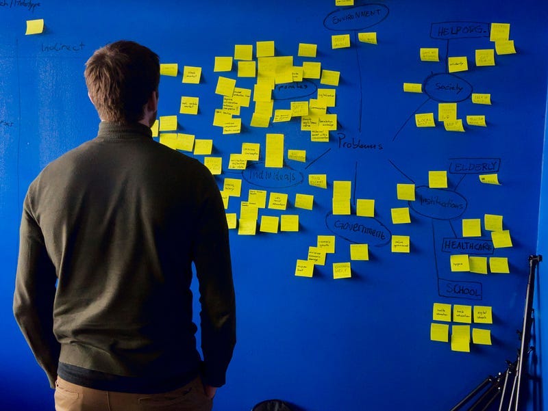 Person looking at a large blue board or wall with sticky notes on it.