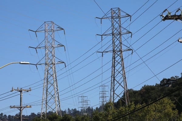Dozens of power lines are strung from several towers and crisscross a clear blue sky. 