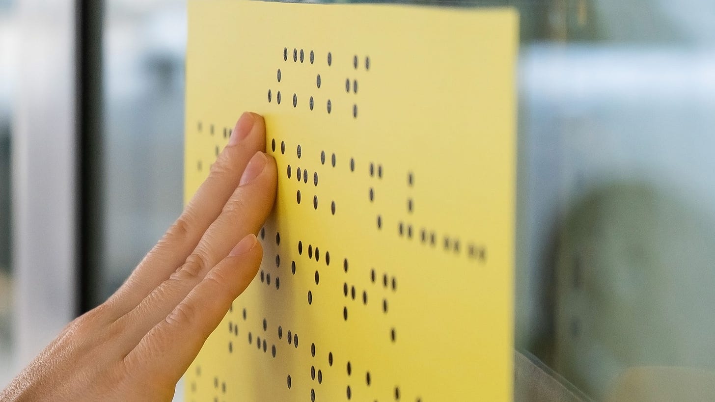 White hand touches yellow sign with Braille