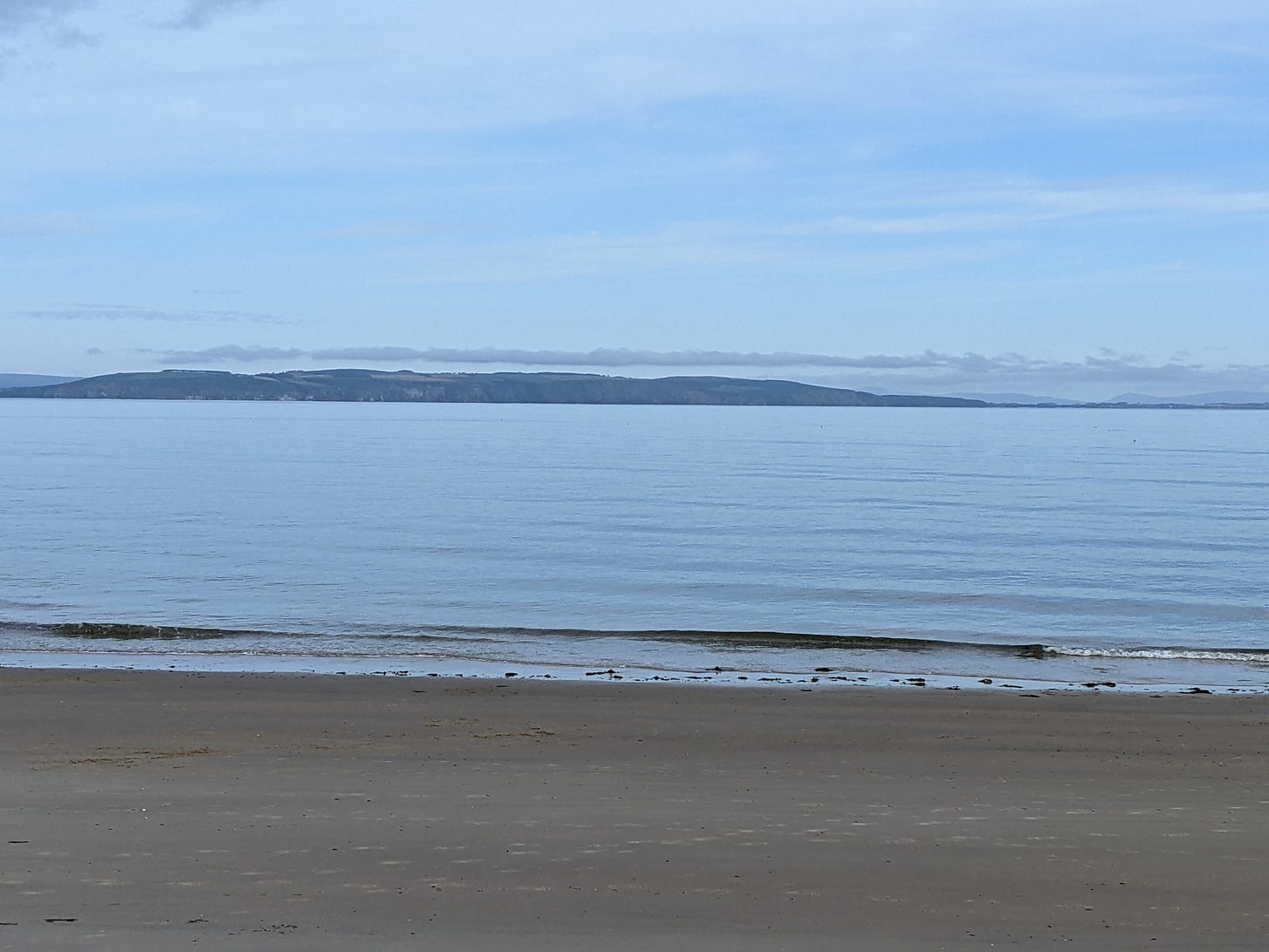 Beach with a calm flat blue sea at Nairn stretching out to the Black isle hills beyond