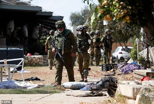 Israeli soldiers walk beside the bodies of Hamas militant killed in Kfar Aza kibbutz on Tuesday
