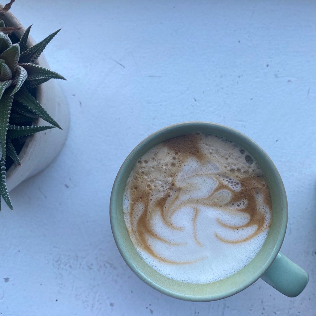 From above, a mint green mug with a latte in it. Dark waves from the espresso are swirled into the white foam on top. Just visible at the upper left edge of the frame is a succulent in a pot.