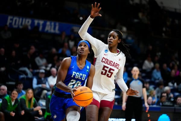 Sha Carter, in a blue F.G.C.U. jersey, shoots the ball while Bella Murekatete, in a white Washington State jersey, lifts her right arm to try to block the shot.