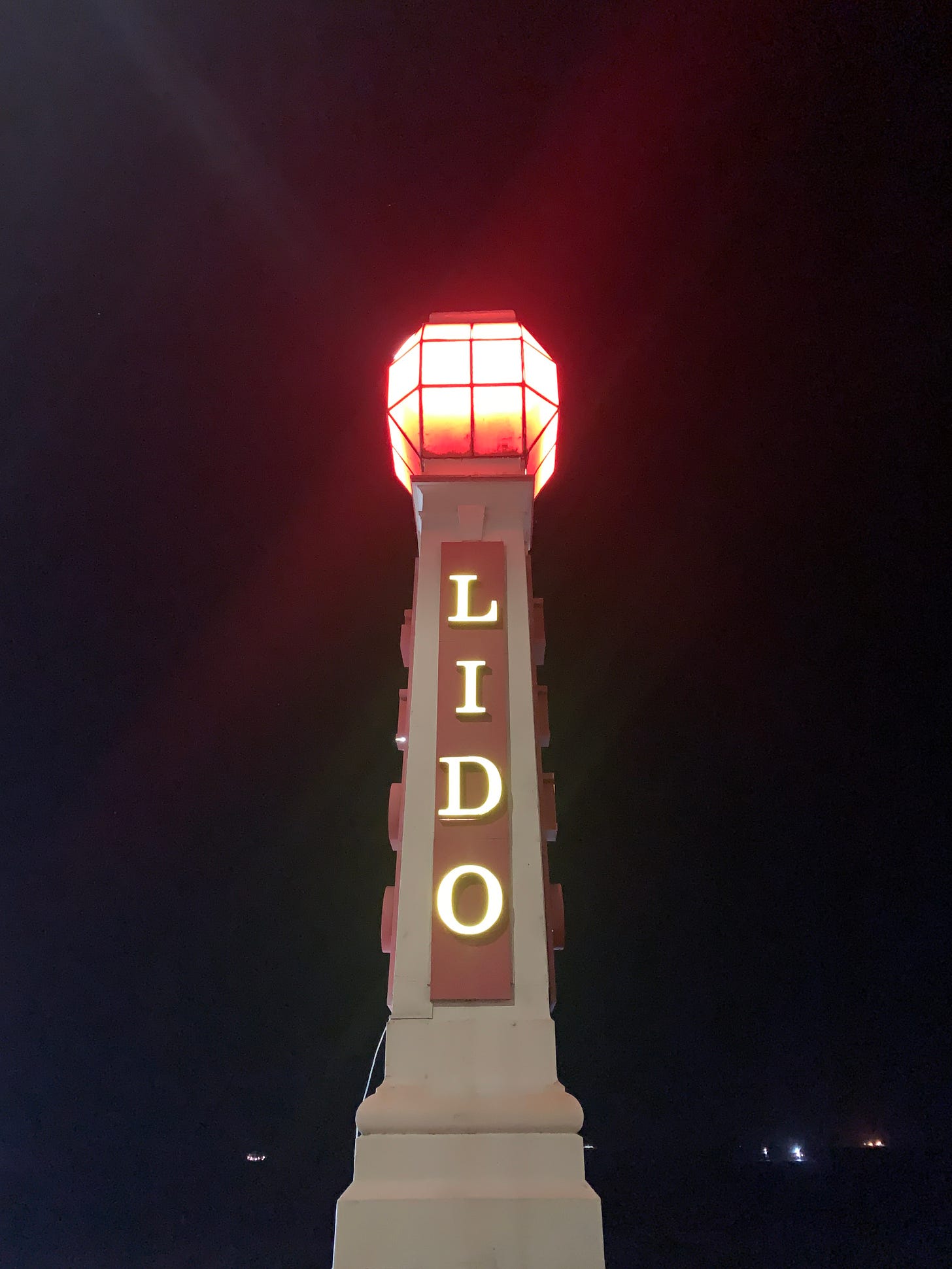 A tall vertical sign reading "Lido" with a red light at the top, and the black night sky as the backdrop