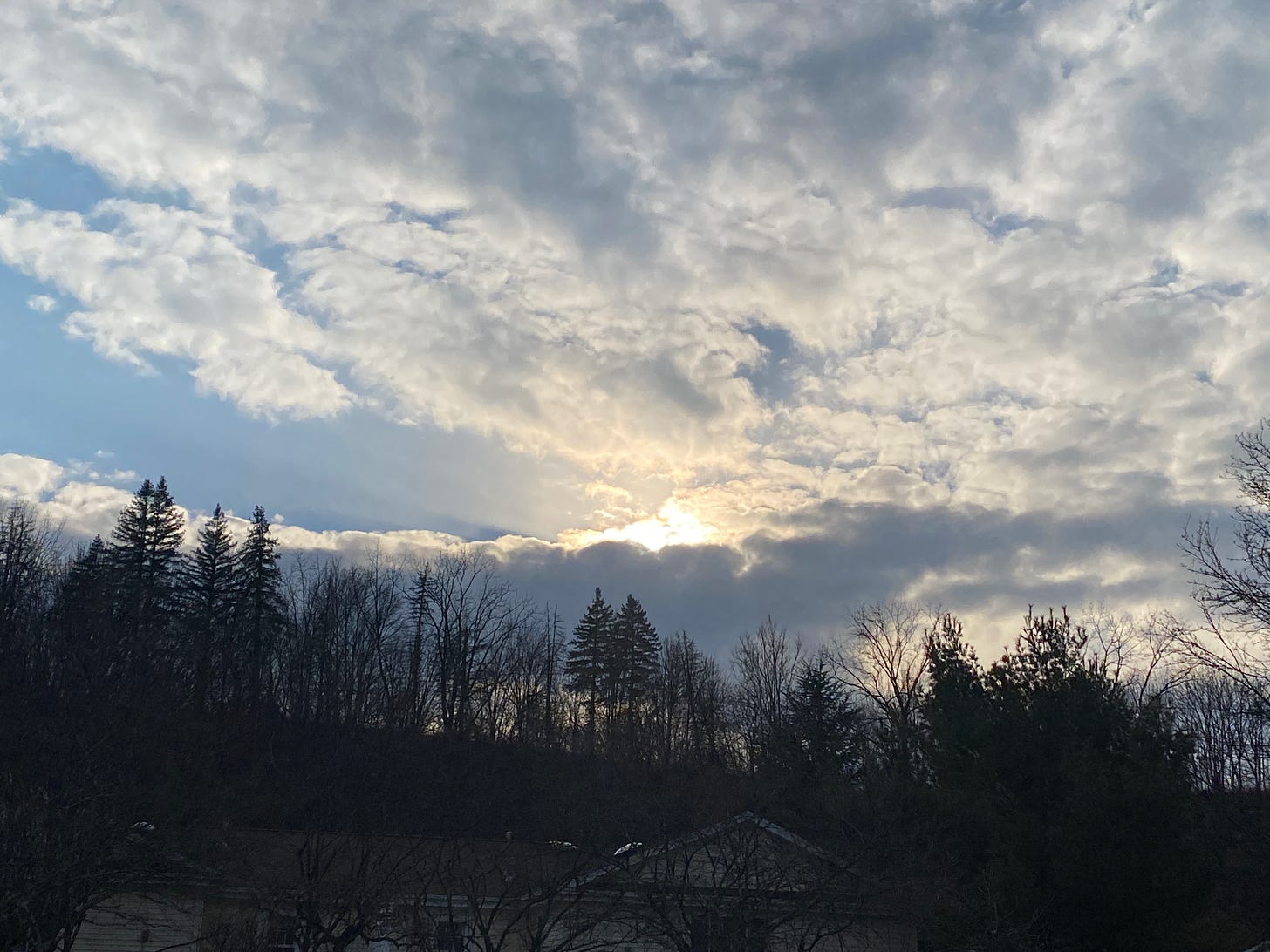 blue sky, billowing white clouds over a hill of trees