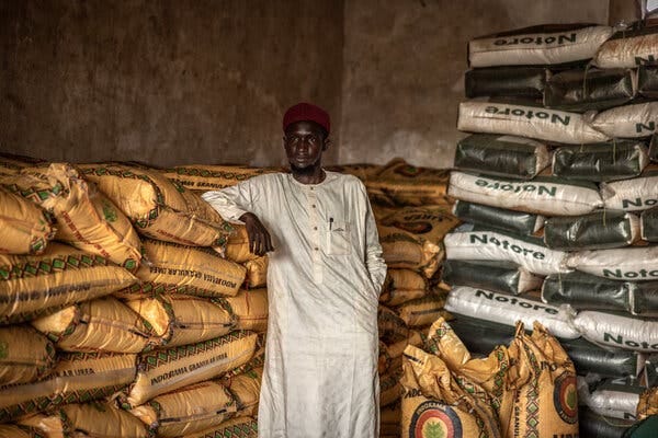 Kasim Abubakar leans against a stack of yellow sacks in a warehouse. 