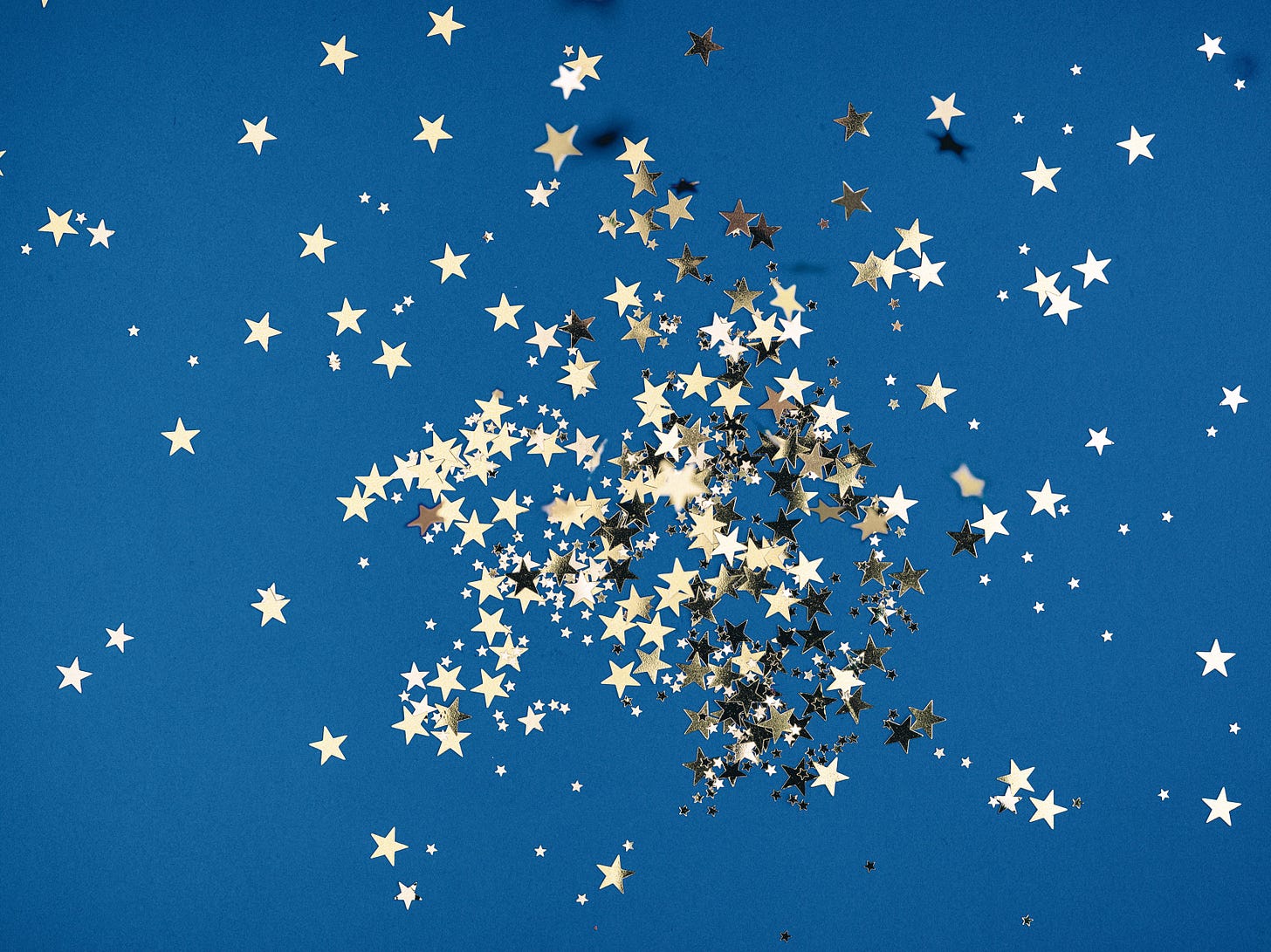A cluster of small, shiny, gold-colored, star-shaped confetti is sprawled across a blue background