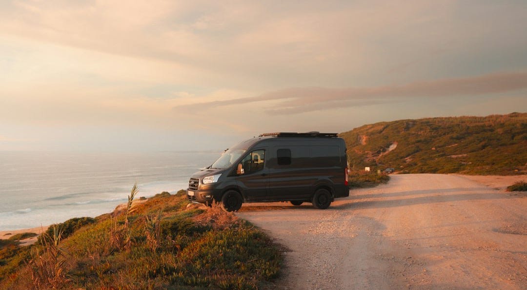 a van driving down a dirt road next to the ocean