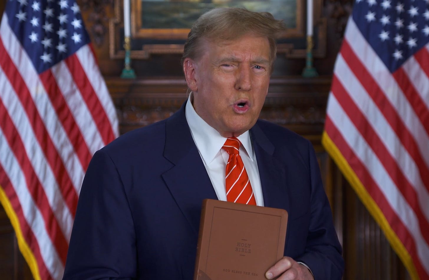 Donald Trump, with flags on both sides of him, holding a brown Bible