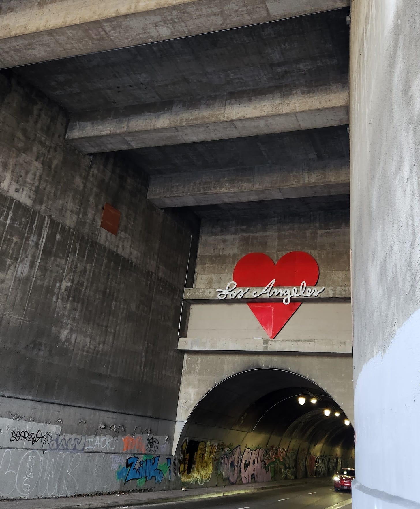 entrance to automobile tunnel with a heart above saying Los Angeles and graffiti on the concrete walls