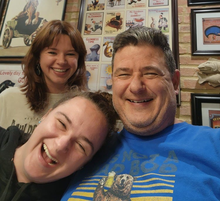 Father laughing with his two 20 something daughters, wall of guiness art in the background