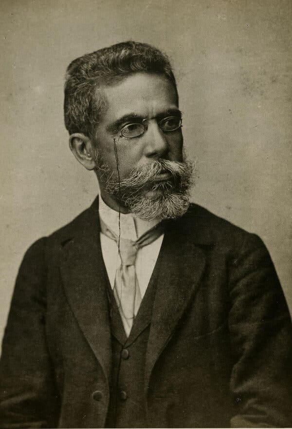 A black-and-white photograph of Machado de Assis, who is wearing a suit and spectacles.