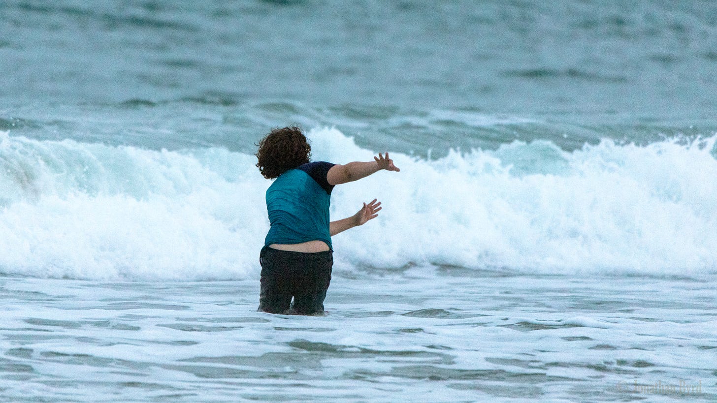 A fully clothed child plays in the ocean. 