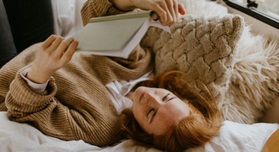 a photo of someone reading in bed and smiling