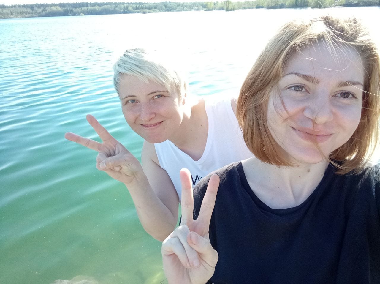 Lena Potyaeva and Seda Suleymanova selfie, doing the victory sign and standing with a pond or river in the background