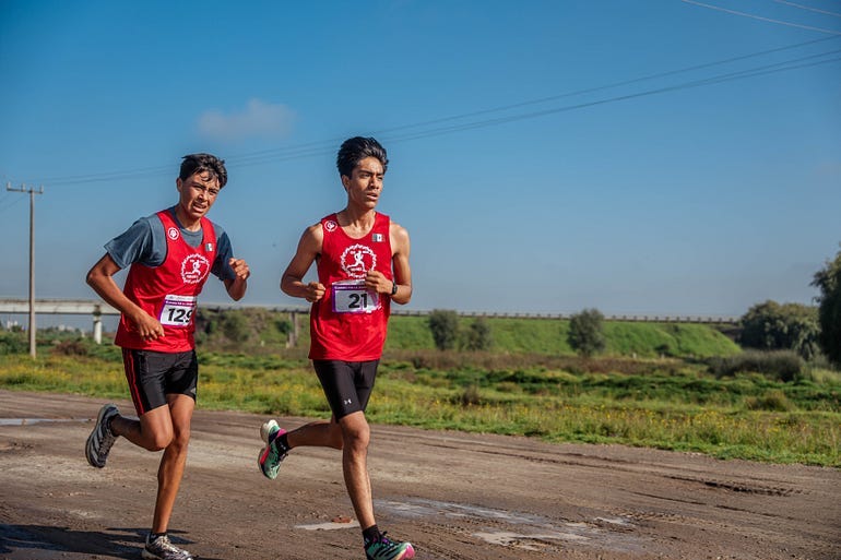 Two men running along the road wearing running uniforms and sweating