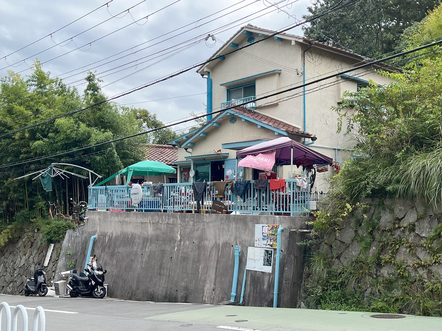 A picture of a quirky cafe in a 1970s Japanese house with a slightly Mediterranean air, clothes hanging on the railings and two mopeds parked outside.