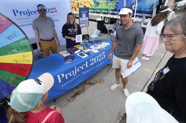 James Bacon, center, talks to fairgoers at the Project 2025 tent at the Iowa State Fair, Aug. 14, 2023, in Des Moines, Iowa. With more than a year to go before the 2024 election, a constellation of conservative organizations is preparing for a possible second White House term for Donald Trump. The Project 2025 effort is being led by the Heritage Foundation think tank. (AP Photo/Charlie Neibergall)