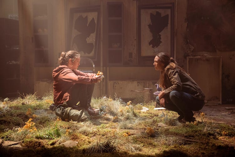 Ellie and Tess talk in a room in a derelict building