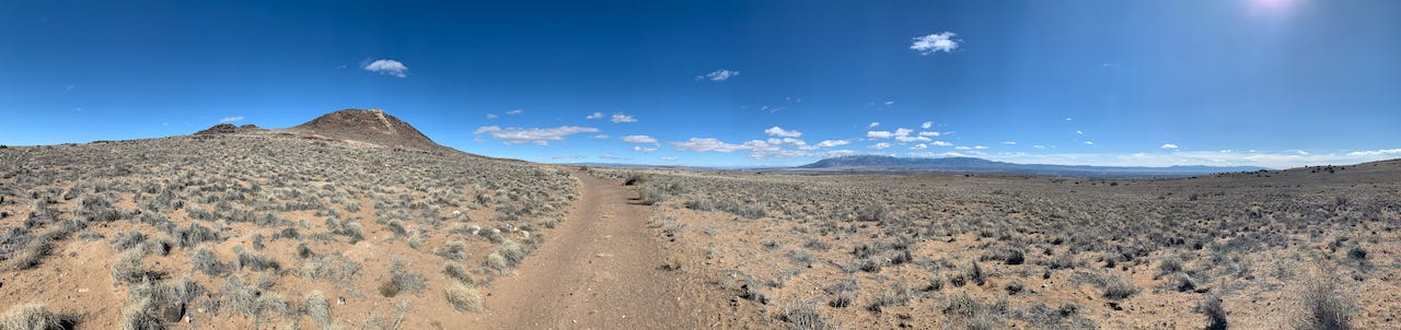 panoramic landscape photo of 3 volcanoes in Albuquerque, New Mexico with deep blue sky, some clouds, and some desert vegetation
