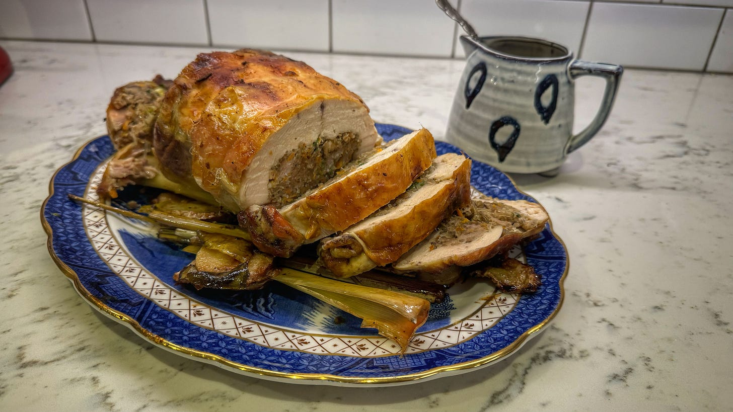 A platter with the finished roast chicken, sliced to reveal the stuffing, with a small pot of coconut milk-based gravy behind it.