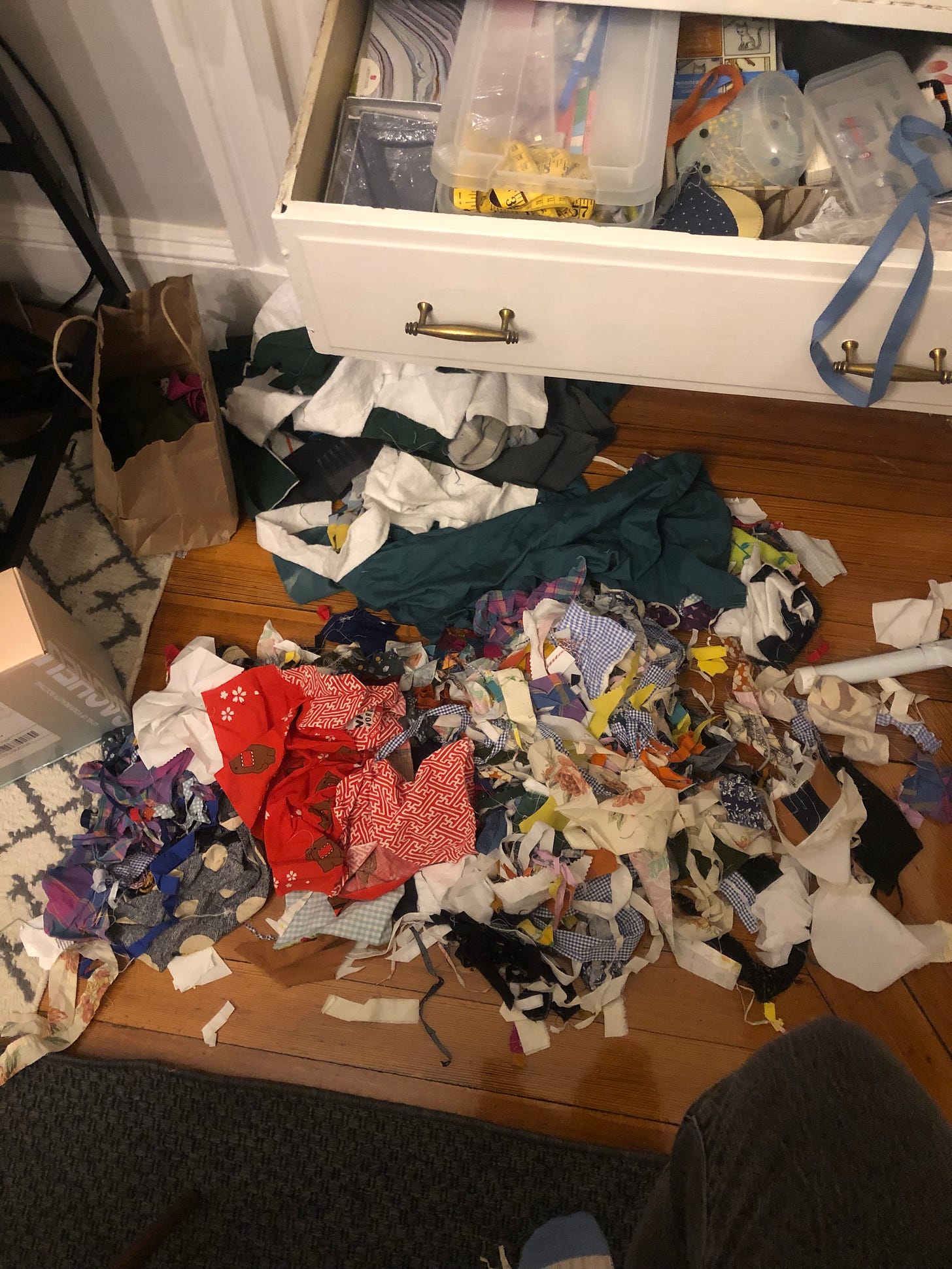 a colorful pile of scraps sits on a wooden floor. behind, a white drawer is ajar