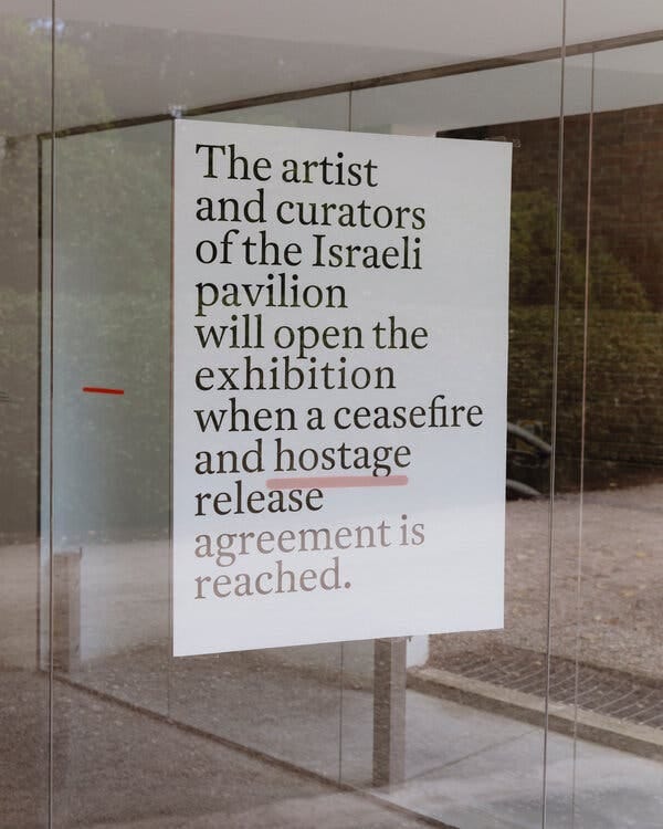 A white sign with black text taped on a window. It reads, “The artist and curators of the Israeli pavilion will open the exhibition when a ceasefire and hostage release agreement is reached.” The word hostage is underlined in red.