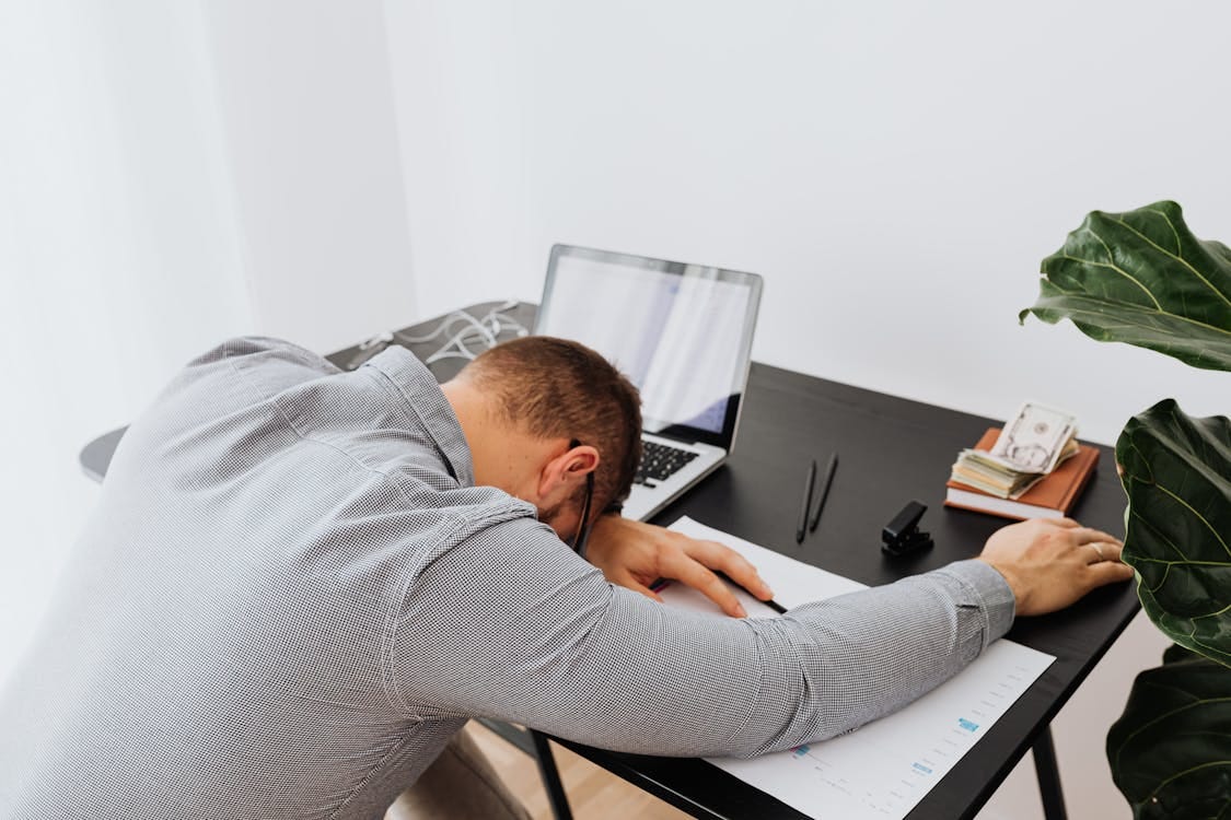 Free Tired man asleep at a desk with an open laptop and paperwork, indoors. Stock Photo