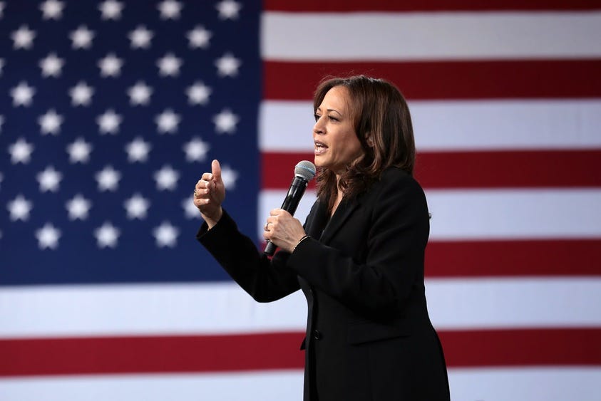 Kamala Harris speaks into a microphone in front of a big US flag