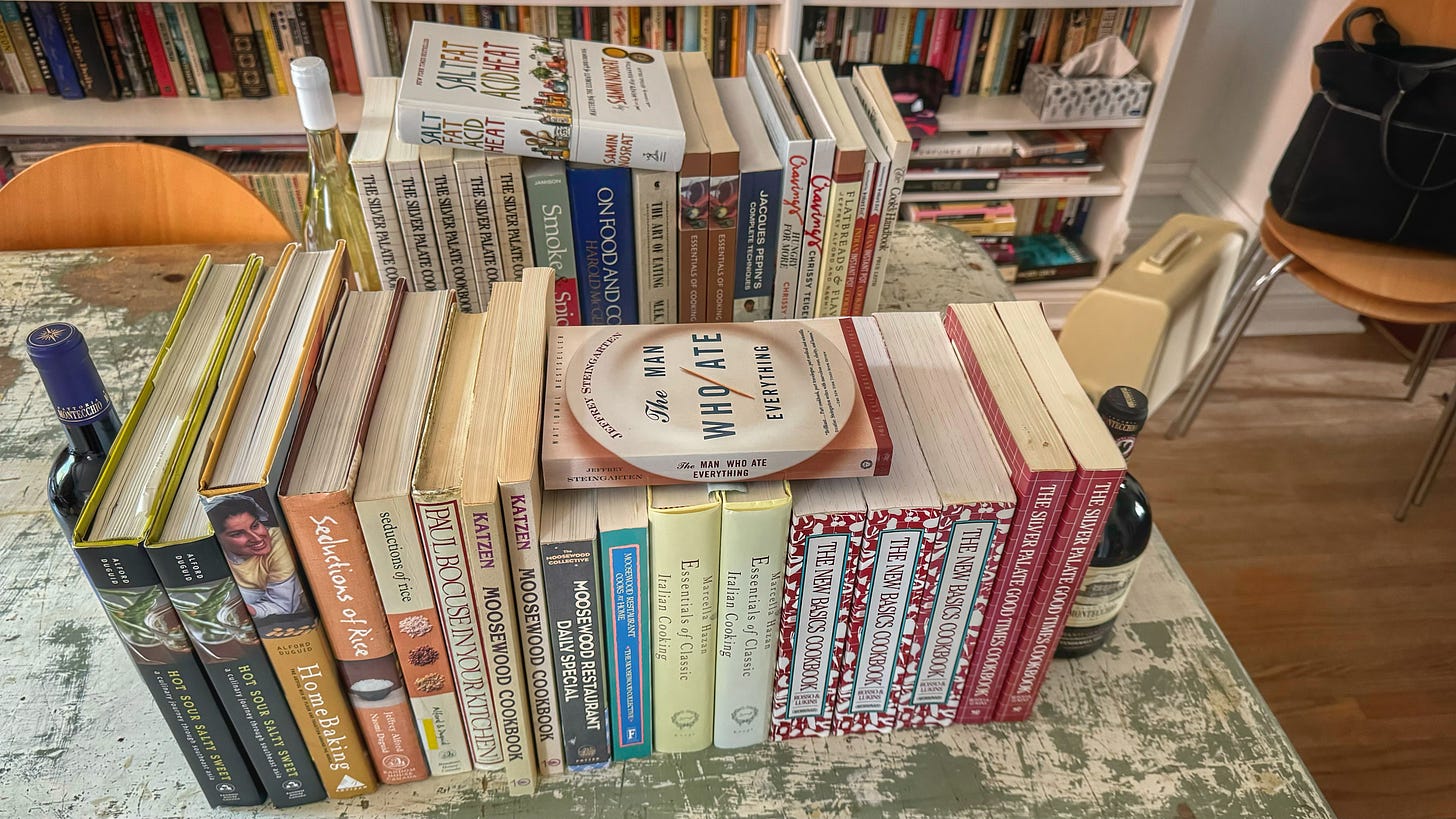 A dining room table with all of the books mentioned in this newsletter, held upright by bottles of wines as bookends