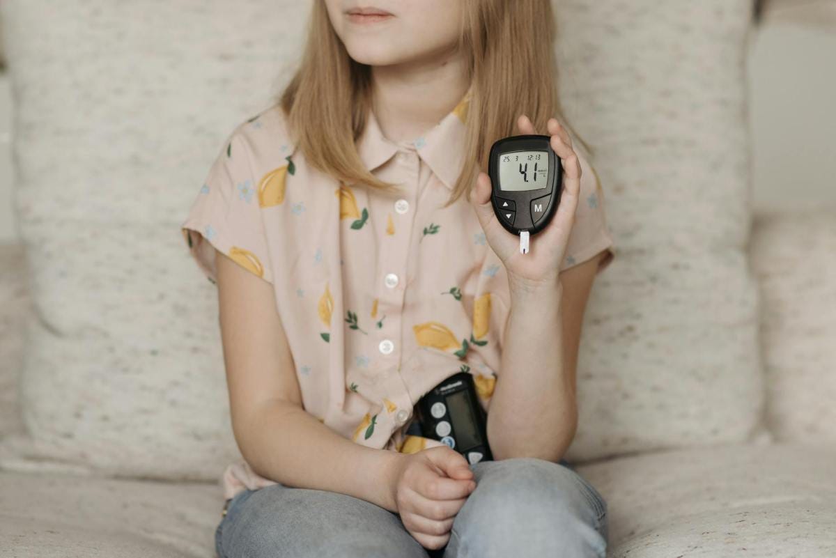 little girl sitting on the sofa and showing her glucometer