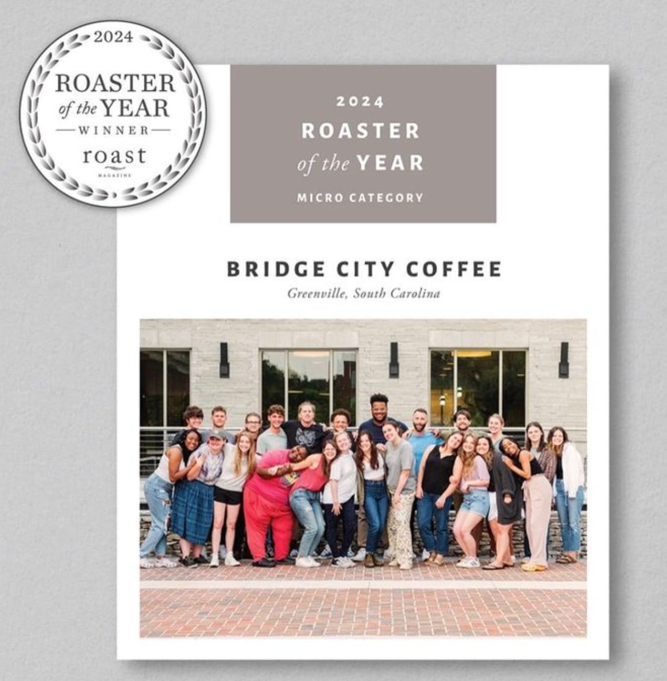 A banner proclaiming Bridge City Coffee the 2024 Roaster of the Year and a photograph of all the employees posing for the photo in front of a white concrete building. An estimated 35 people are smiling at the camera.