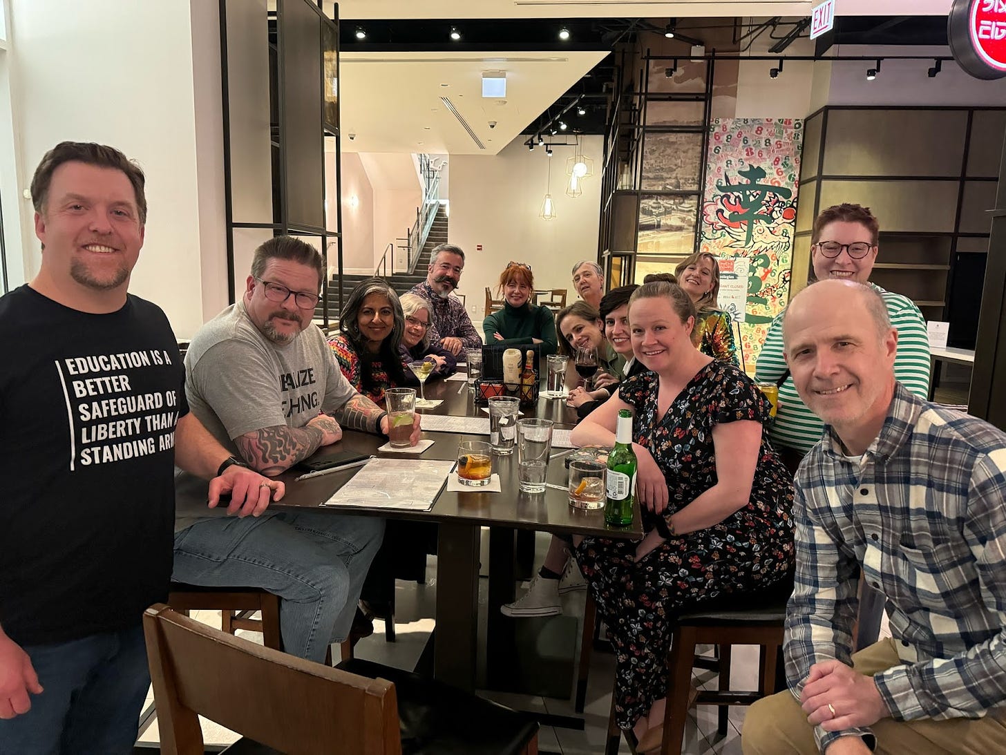 A group of 13 educational developers (including Emily and Josh) at a long bar table, smiling for the camera.