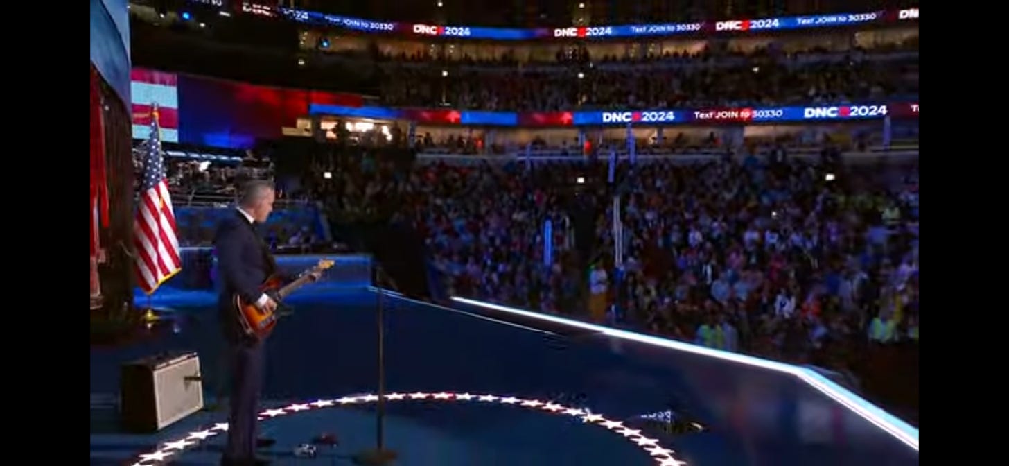 Jason Isbell stands on the stage of the DNC, with his guitar and a small amp behind him, with a view of the audience in front of him