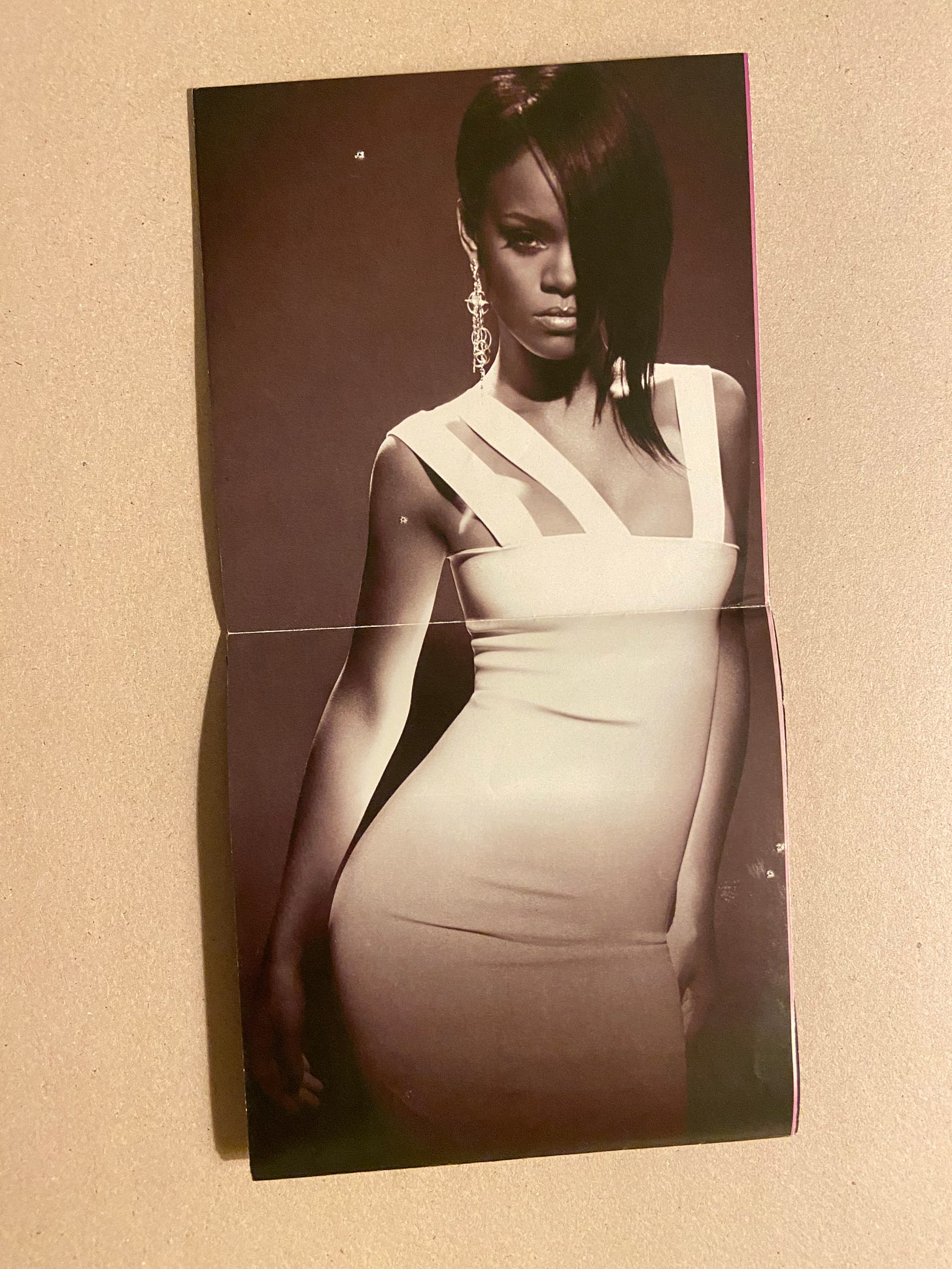 Rihanna serving b&w CoverGirl vibes in a photo from her Good Girl Bad album; she wears a white bodycon dress, dangly earrings, and her bangs cover her left eye.