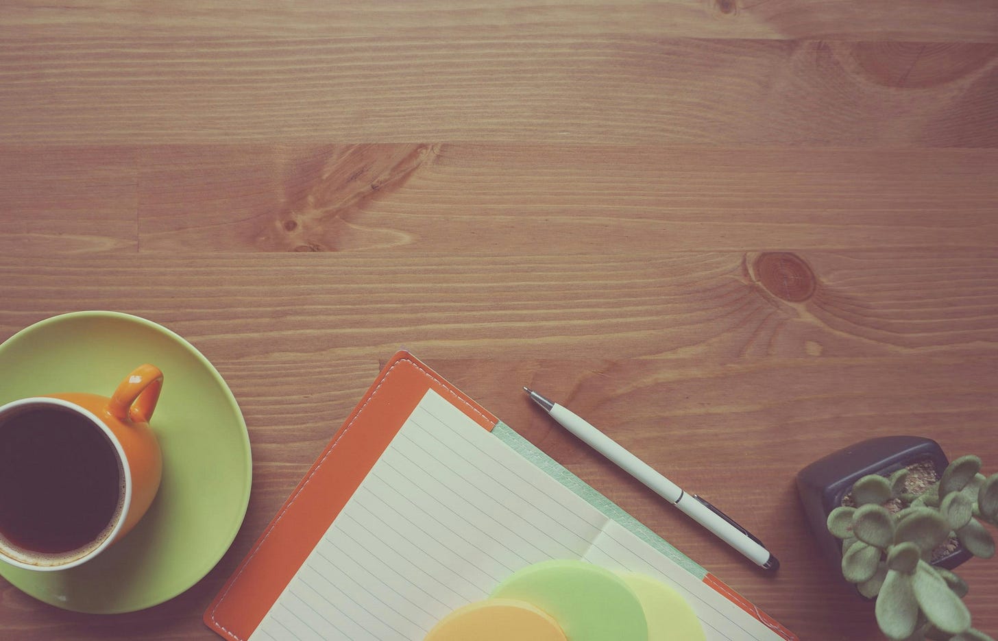 Desk with coffee, notebook, pen, and potted plant