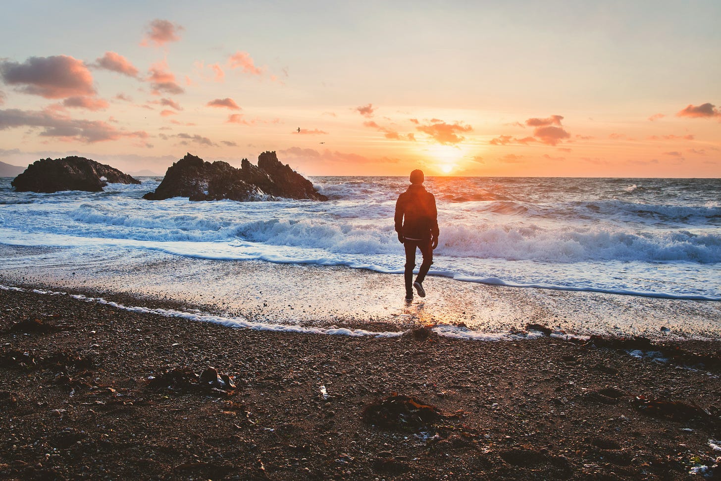 Image of a man walking on a beach at sunrise.