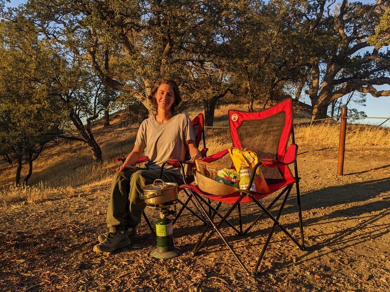 Rey sitting in a camp chair with propane stove and dinner supplies 