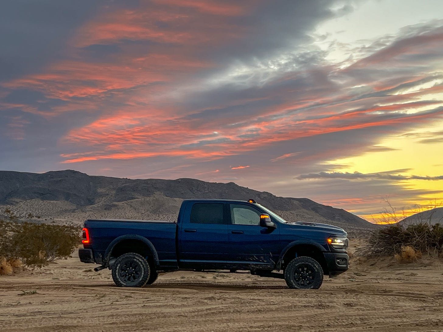 Side view of a blue Ram 2500 Power Wagon parked in the desert against a pink, orange and yellow sunrise overhead.