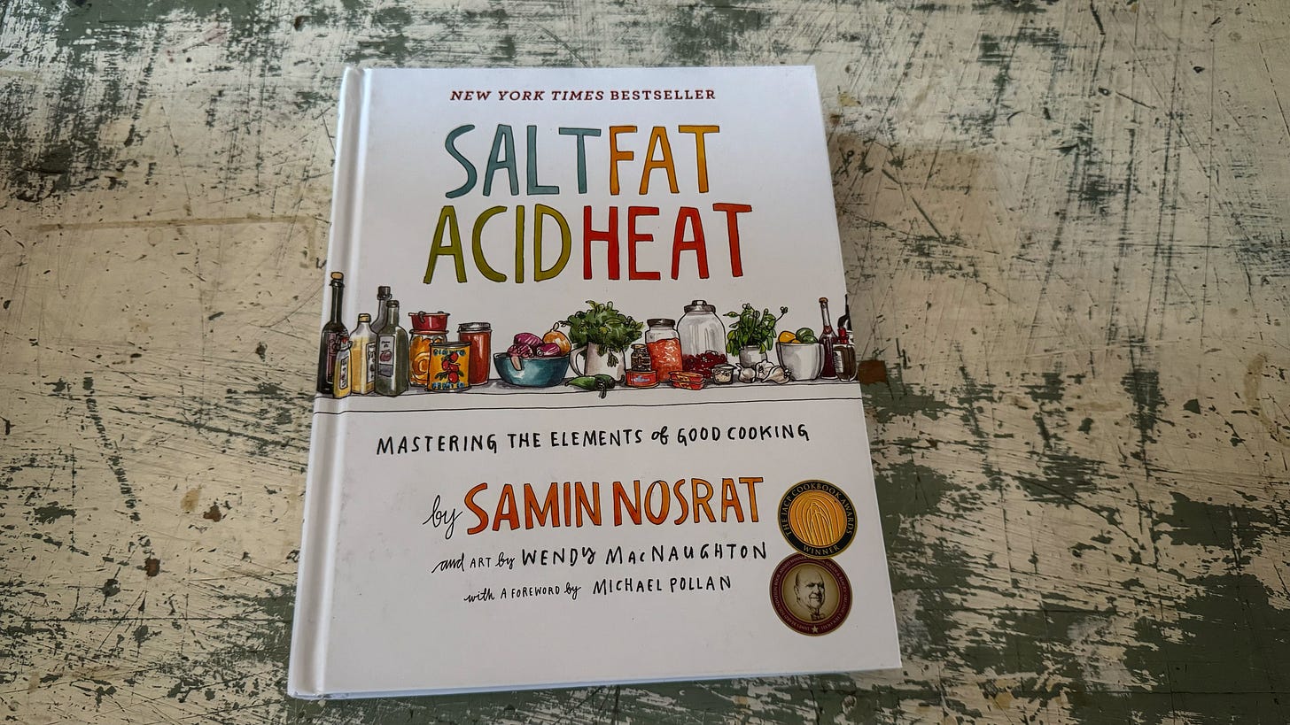 A hardcover copy of Salt Fat Acid Heat, subtitled "Mastering the Elements of Good Cooking"