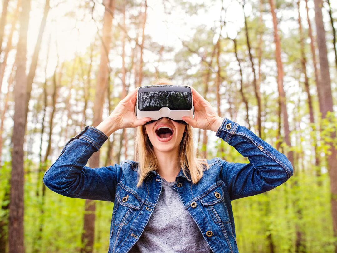 Woman wearing virtual reality goggles while outside, surrounded by a beautiful forest scene.