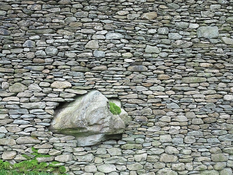 Massive dry-laid stone wall with one huge rock incorporated in the structure.