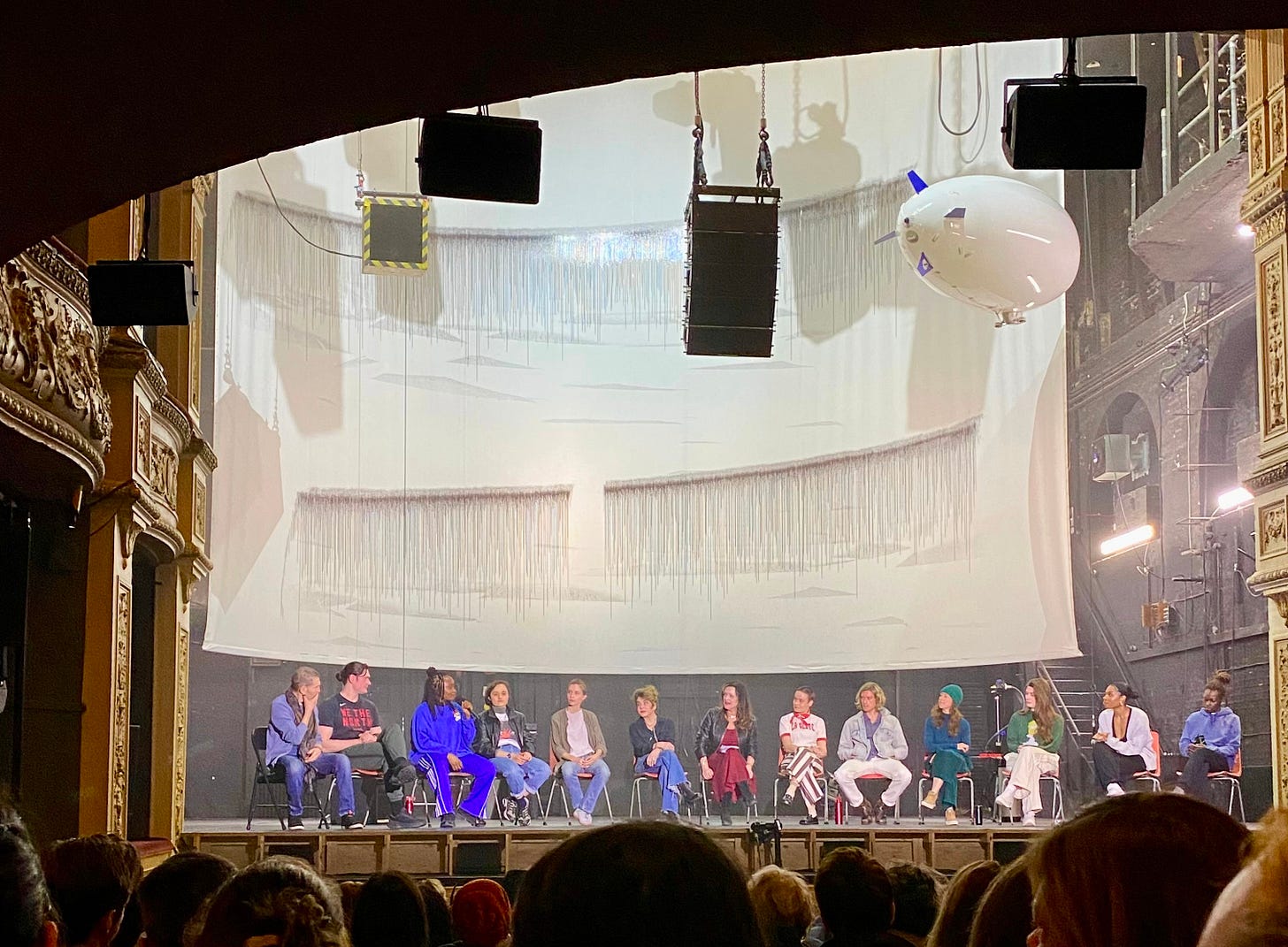 The cast of Elektra on set with classics scholar Edith Hall, the show’s blimp suspended overhead like an all-seeing god. The cast of Elektra on set with classics scholar Edith Hall, the show’s blimp suspended overhead like an all-seeing god.