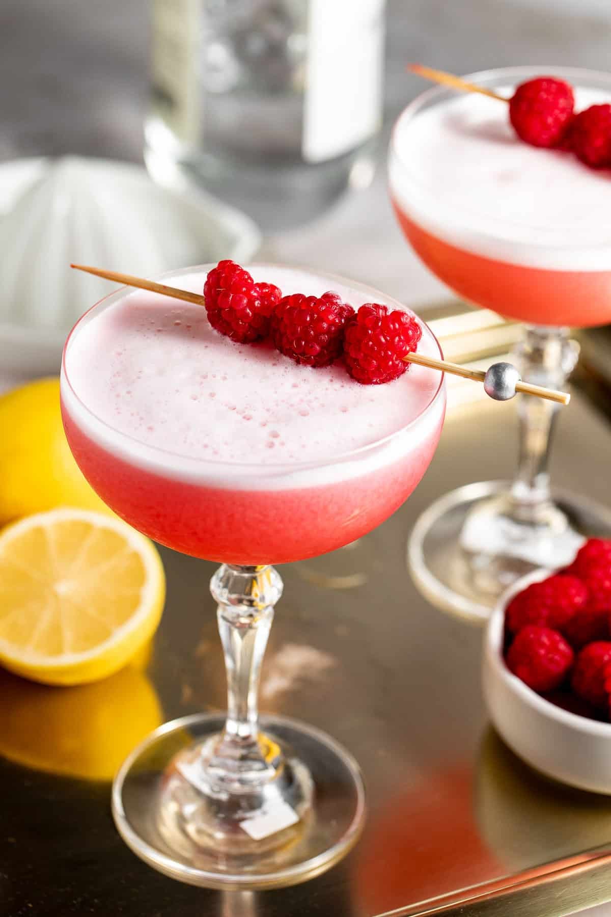 two glasses on gold tray with raspberries