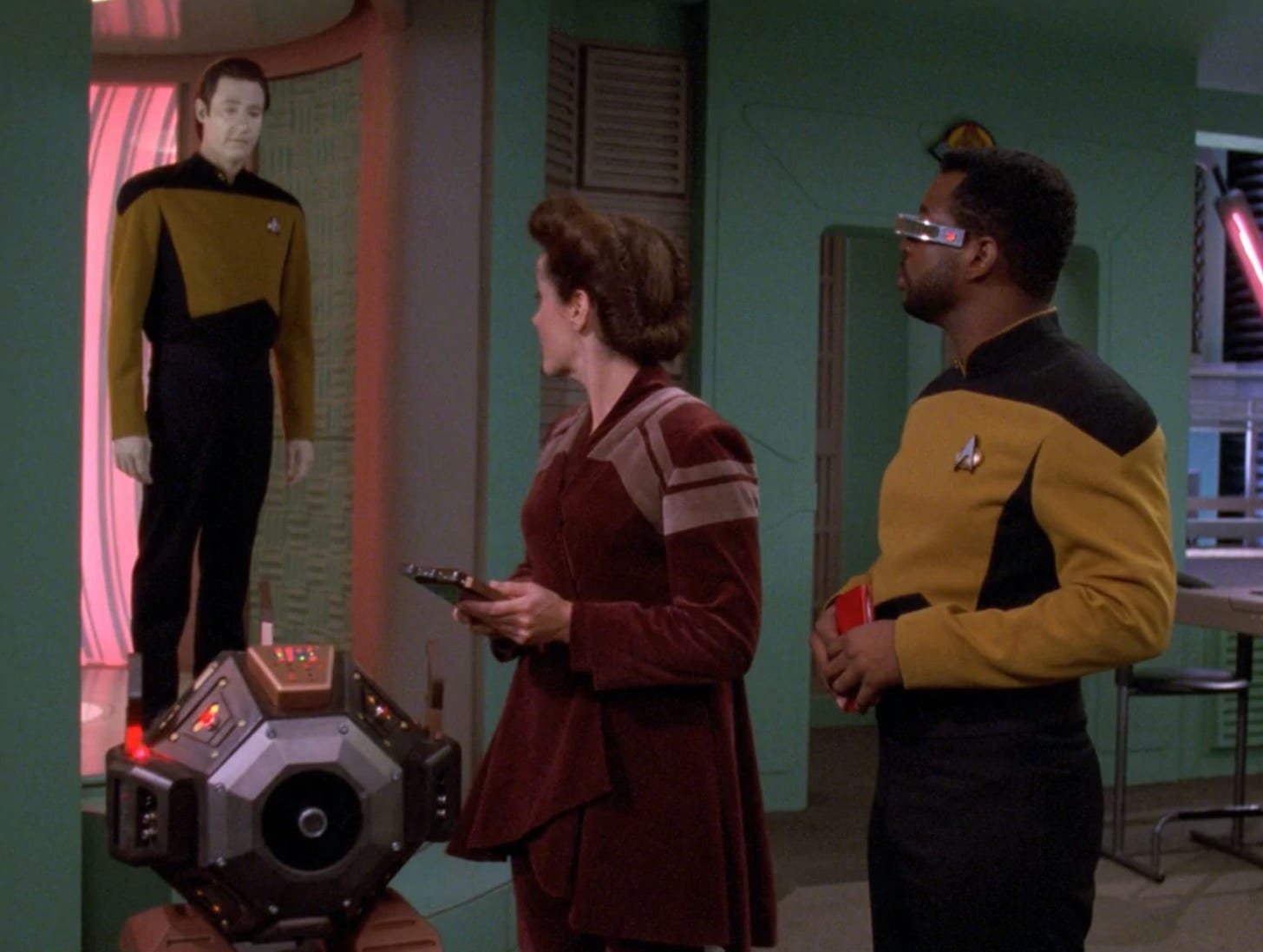A frame from the Star Trek The Next Generation episode "Quality of Life," in which the android Commander Data stands near an octagonally-shaped robot, about to tell two other humanoids to stop using the robot for labor, since it might be alive.