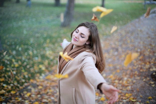 white woman with jacket dancing in leaves