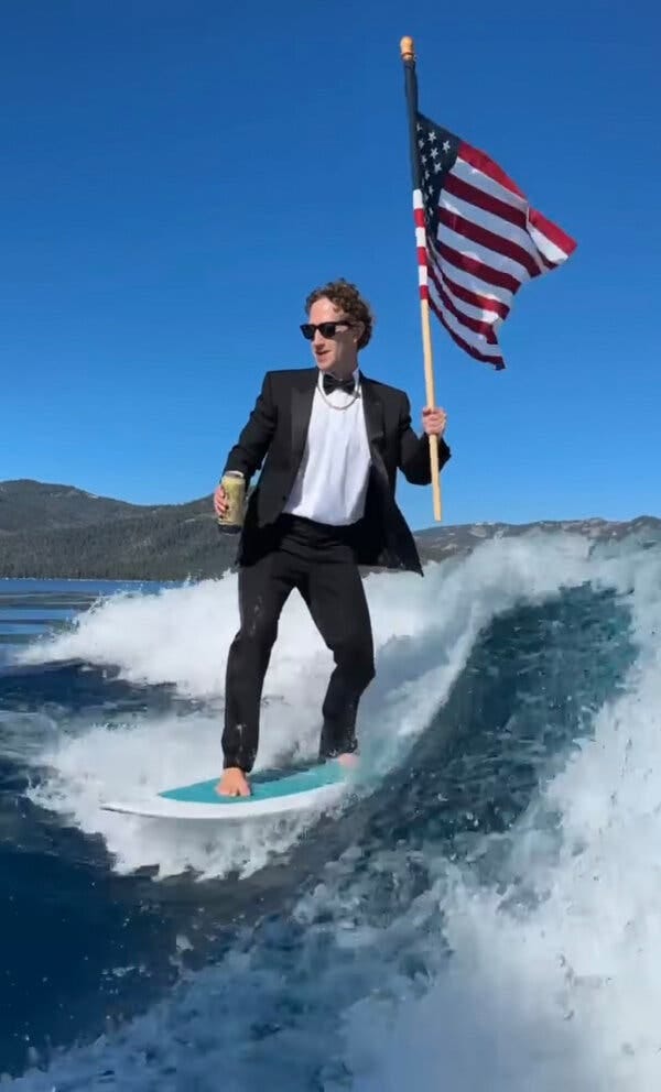 In a video still, Mark Zuckerberg holds an American flag while wearing a tuxedo and riding a surfboard in a boat’s wake. In his right hand he is holding a can of beer.